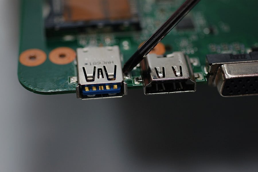 Pemeriksaan jarak dekat pada titik solder dan konektor port di papan sirkuit motherboard laptop di workshop HARDCARE.