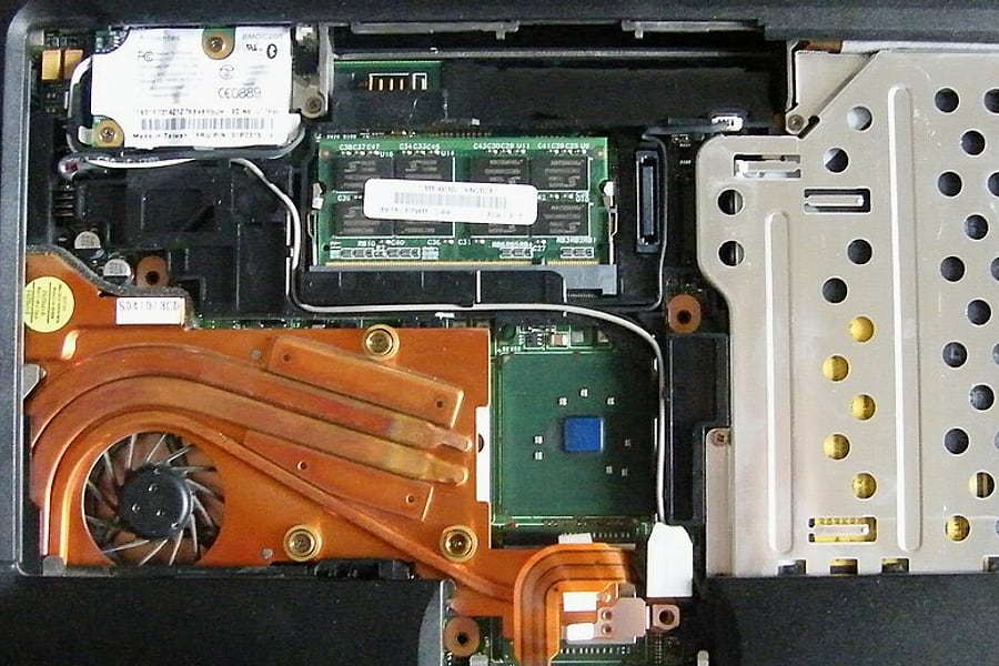 Susunan internal laptop memperlihatkan keping memori SO-DIMM RAM pada slotnya serta rakitan pipa pendingin tembaga di meja upgrade HARDCARE.